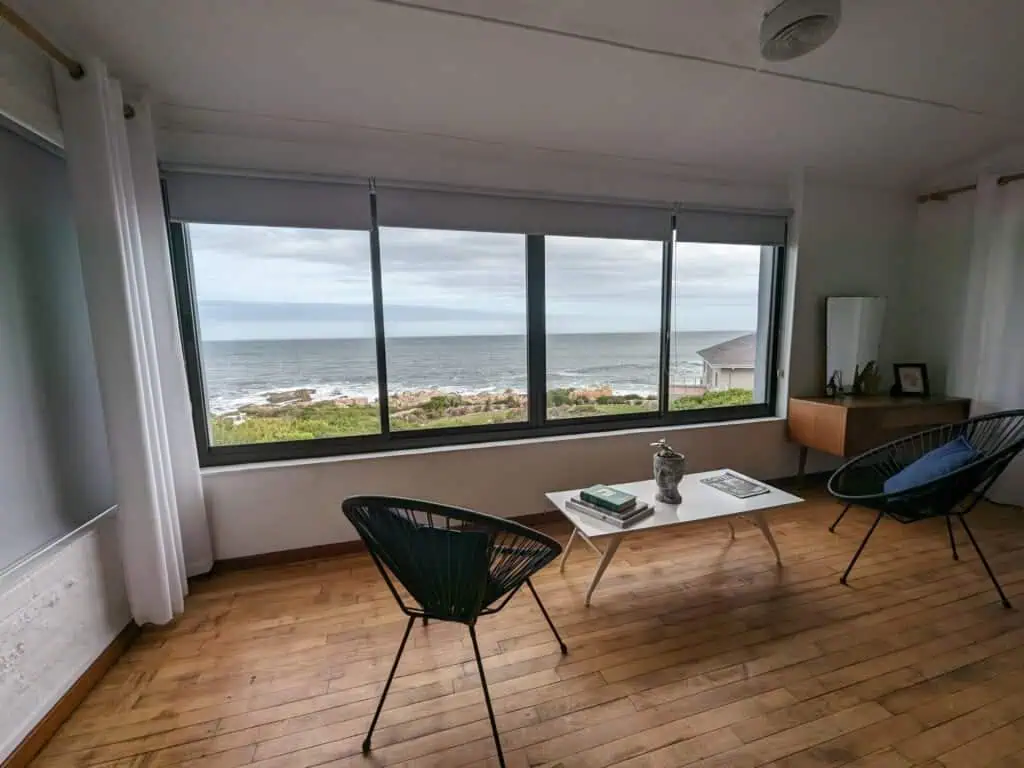 Serene ocean view from a cozy coastal room featuring large windows, wooden flooring, and modern furniture, perfect for a relaxing Afrique safari experience.