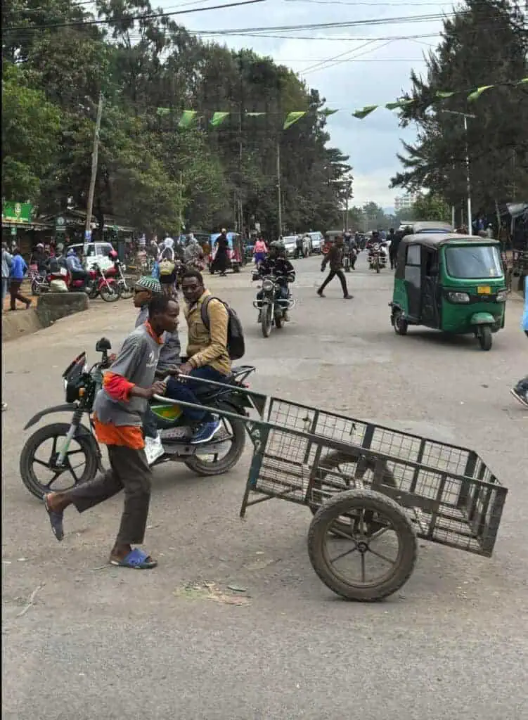 A crowded street scene in Africa with motorbikes, tuk-tuks, pedestrians, and market stalls, showcasing vibrant local urban life and transportation methods in an African city.