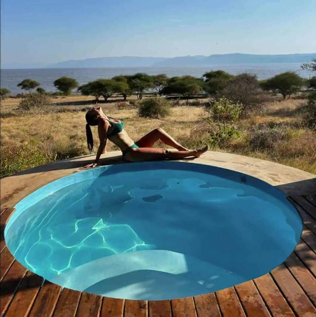 Relaxing woman lounging by a hot tub overlooking the African savannah and distant water body, perfect for luxury safari travel experiences in Africa.