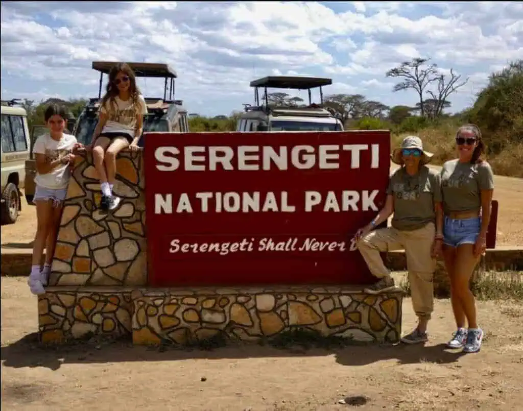 Vibrant group photo at Serengeti National Park entrance with safari vehicles, showcasing adventure and wildlife exploration in Tanzania's iconic safari destination.