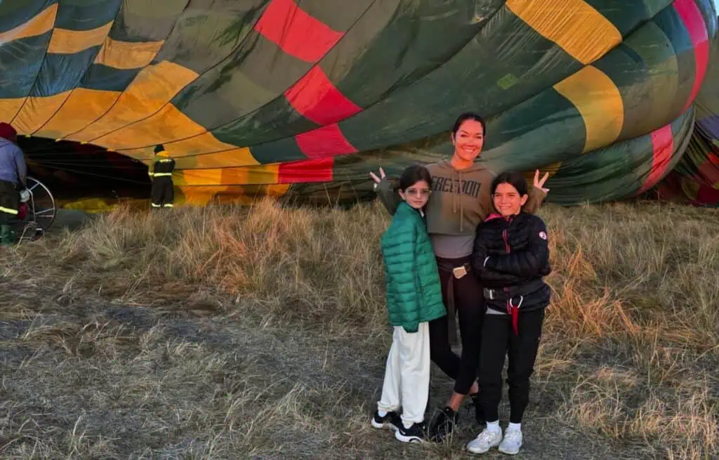 Hot air balloon preparing for takeoff in the African savannah with people standing nearby.