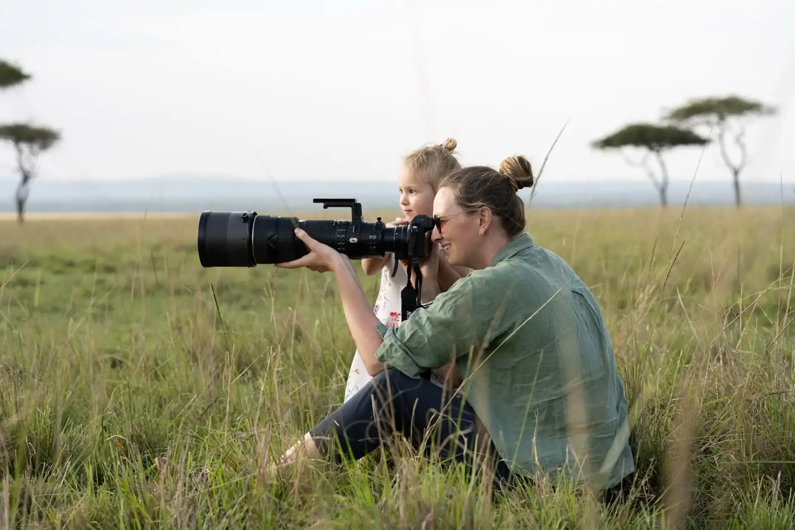 Woman and child on safari in African grassland, observing wildlife through a telescope, capturing nature's beauty and adventure.