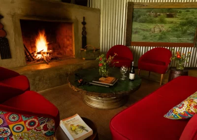 A warm and inviting safari lounge featuring a lit fireplace, vibrant red seating, and decorative cushions, perfect for relaxing after a day of exploring Africa's wildlife.