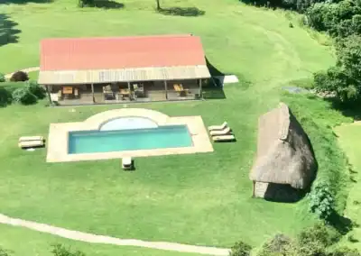 Aerial view of a luxury safari lodge in Africa featuring a swimming pool, a thatched-roof hut, and lush green surroundings, perfect for an authentic African safari experience.