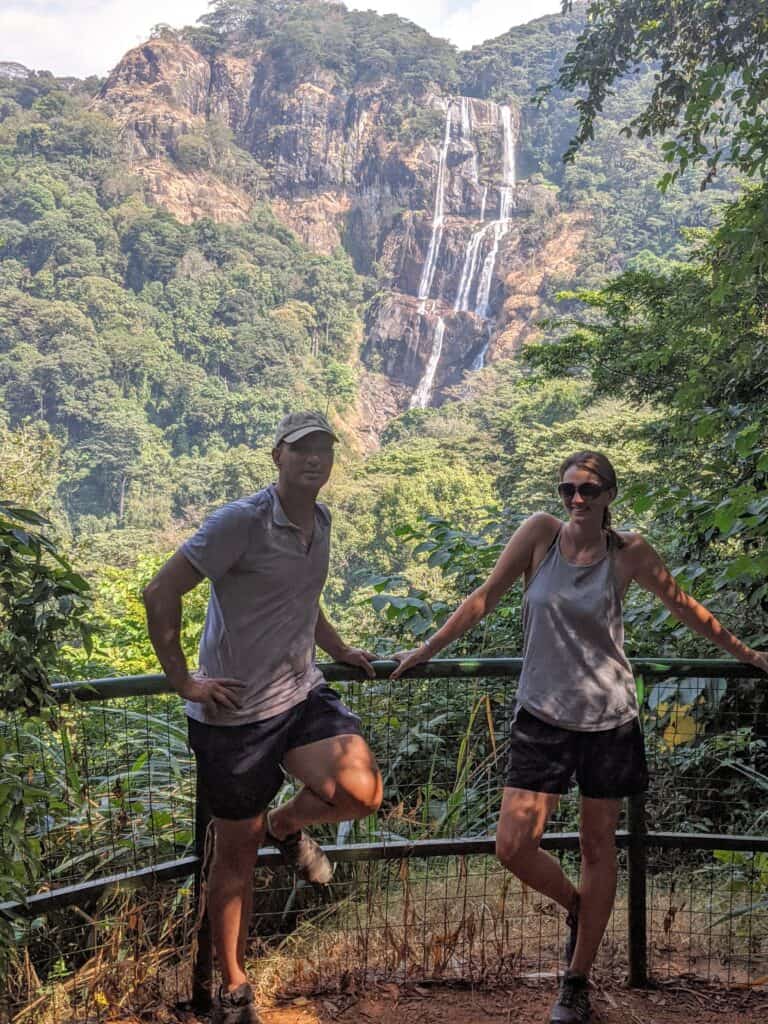Me and my husband standing at a viewpoint in front of a tall waterfall in Udzungwa National Park, Tanzania