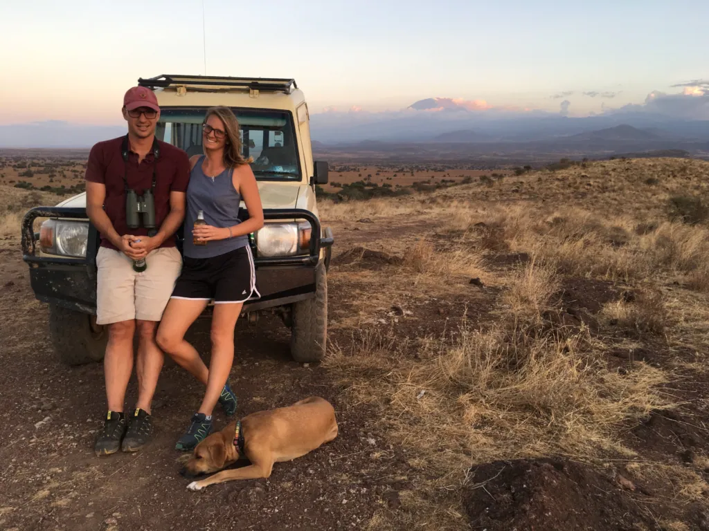 Me and my husband leaning on a Land Rover with our dog, with Mount Kilimanjaro in the distance at Enduimet, Tanzania