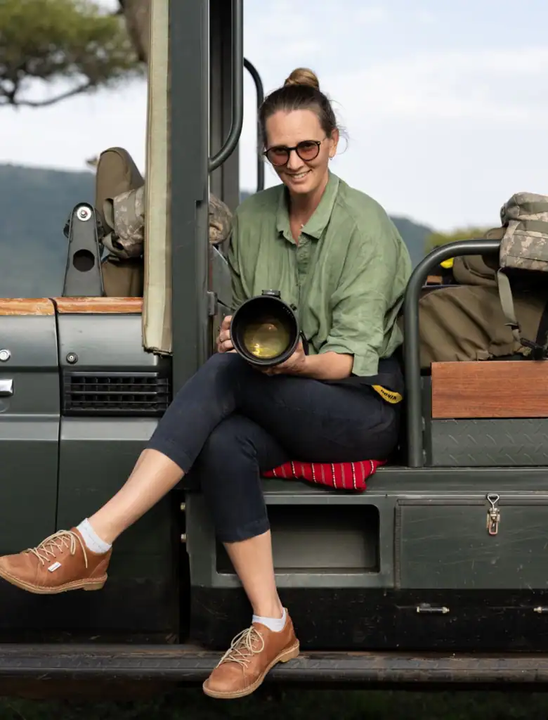 Me sitting on the side of an open safari vehicle in a green shirt, holding a camera with a long lens