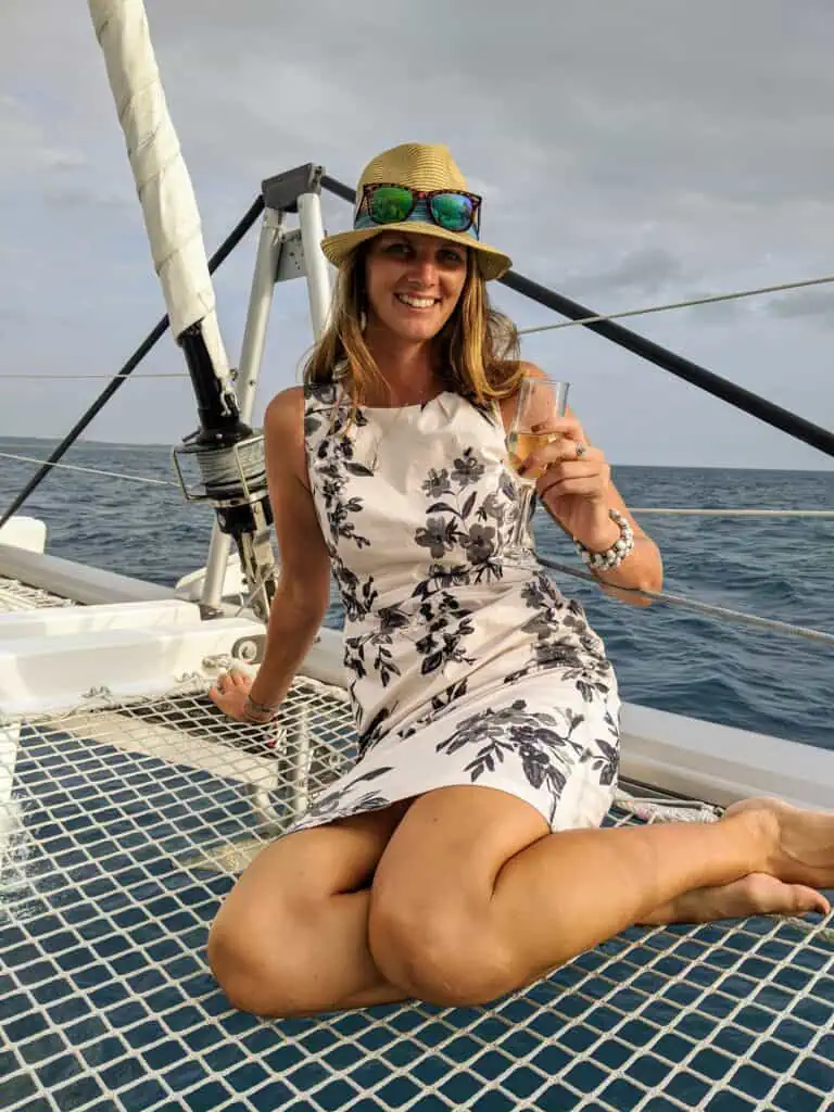 Me in a straw hat and floral dress sitting on the deck of a catamaran with the sea behind me, on a yacht cruise off Zanzibar