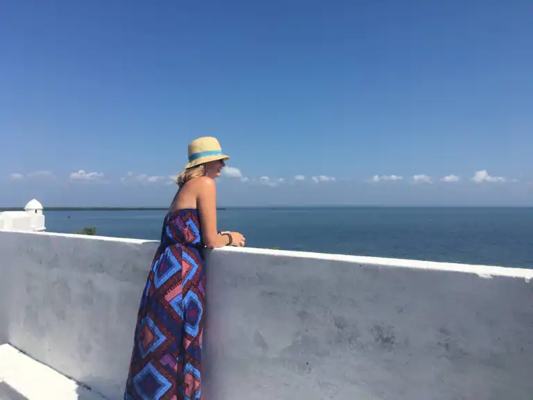 Me in a sun hat and patterned dress looking out over the sea from a whitewashed wall in Mozambique