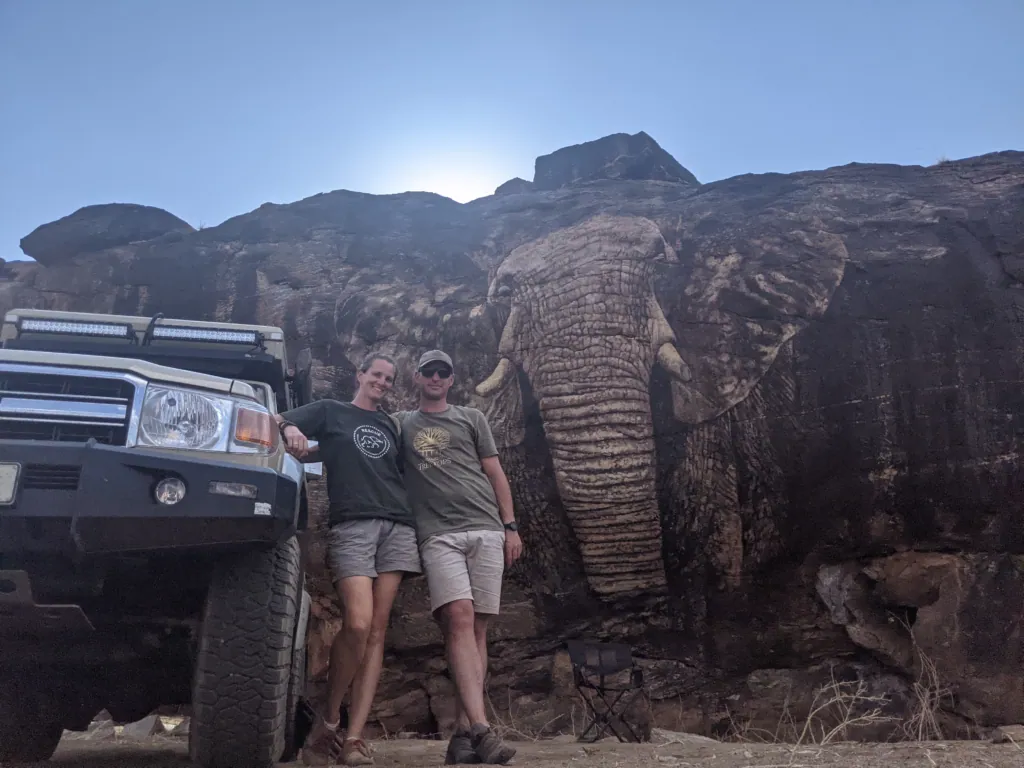Me and my husband standing beside our safari vehicle in front of a great rock formation shaped like an elephant at Reteti, Kenya