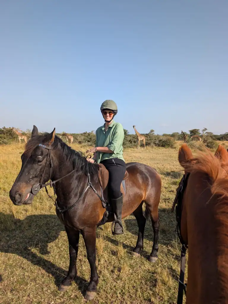 Me on horseback in Enonkishu Conservancy with giraffes standing in the grassland behind me, Maasai Mara, Kenya