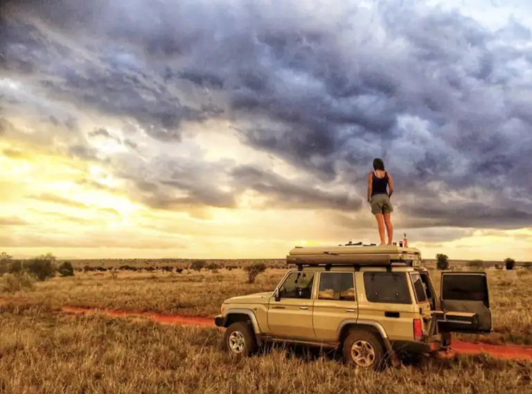 Me standing on the roof of our safari vehicle under a stormy sunset sky in Tsavo, Kenya